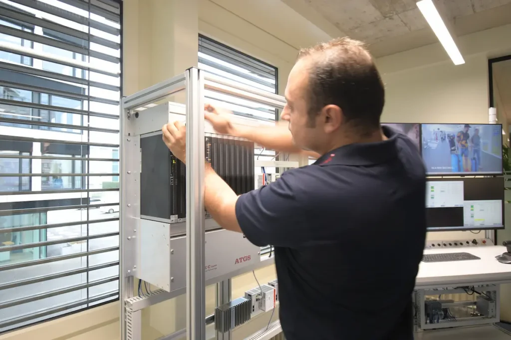 Ein Inautec-Ingenieur arbeitet an einem ATGS-Steuerungsrack mit redundanten Modulen und Diagnose-Bildschirmen zur Gewährleistung maximaler Anlagenverfügbarkeit in Wollerau, Schweiz.