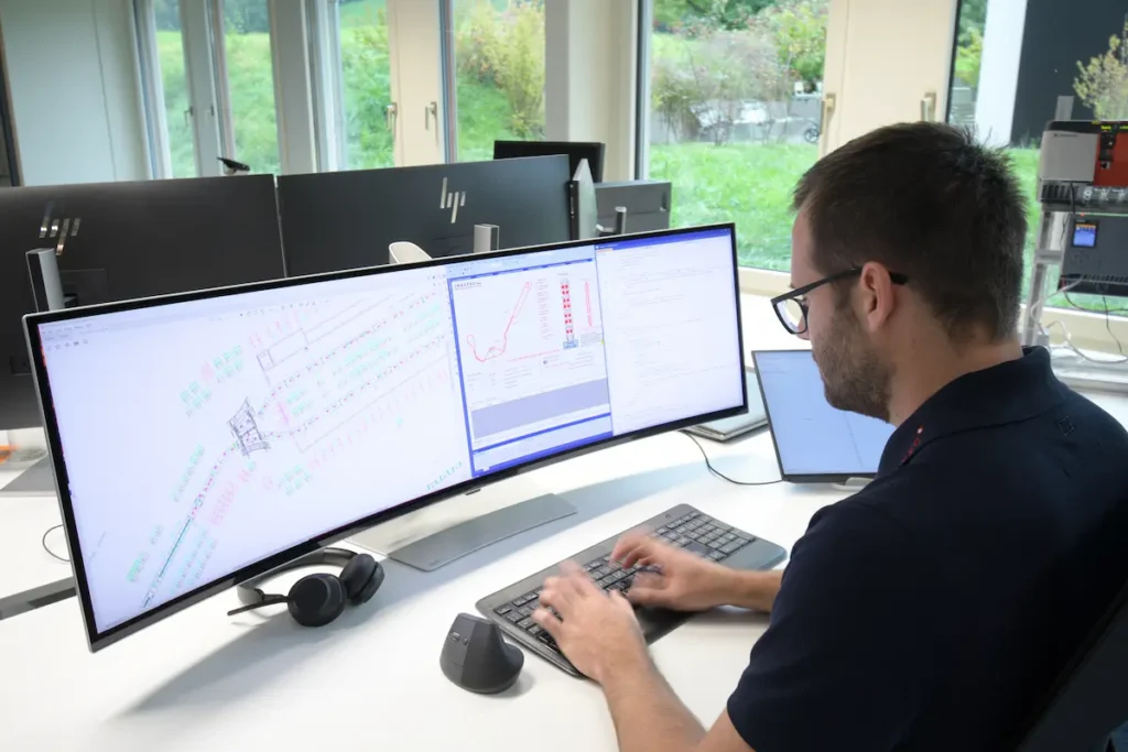 Ein Inautec-Ingenieur entwickelt CAD-Layouts und Steuerungscode für Personentransportanlagen an einem Ultrawide-Monitor im Entwicklungsbüro in Wollerau, Schweiz.